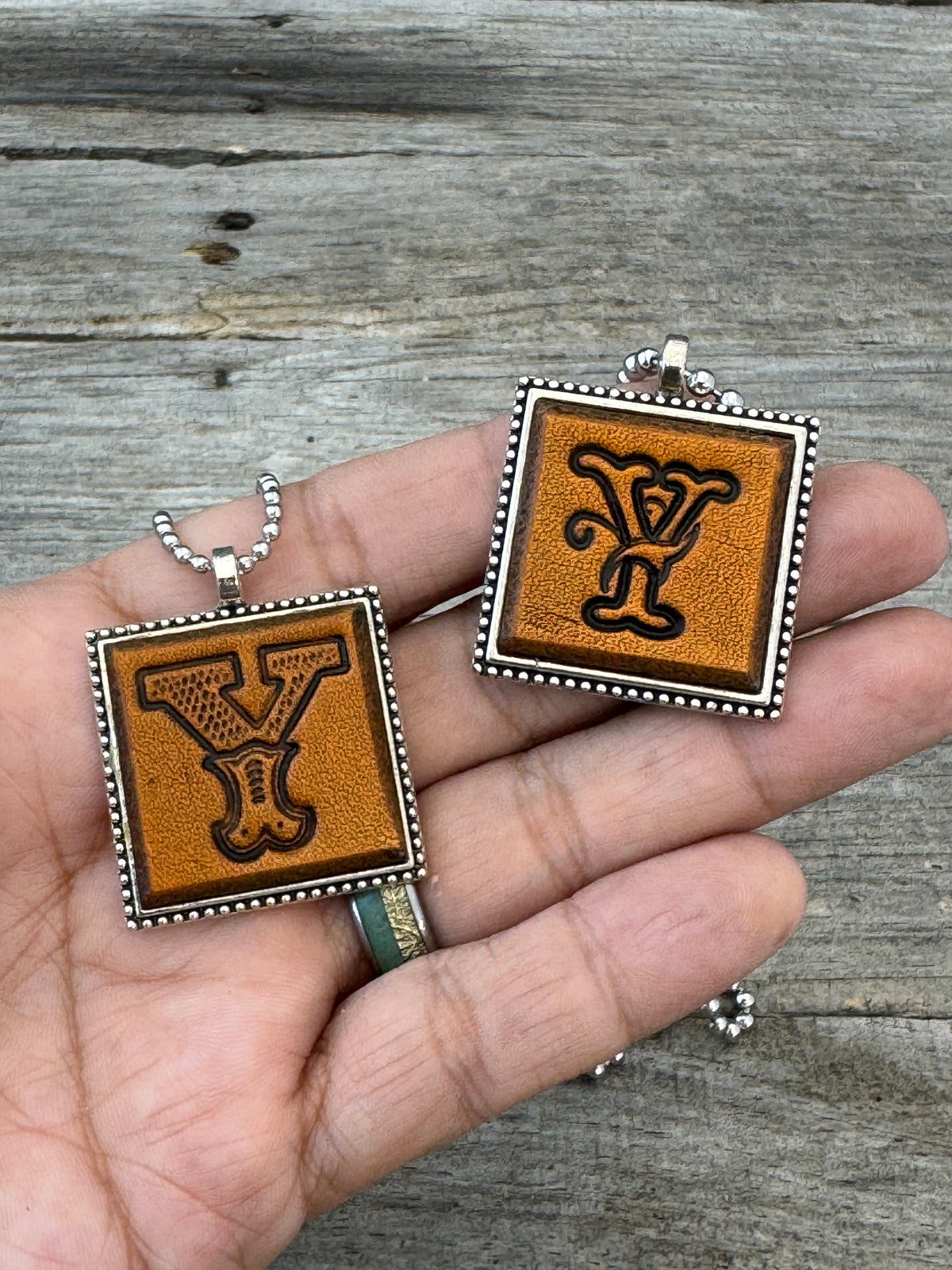 Western Block and Floral Script Letter Y leather necklaces held in hand for size comparison