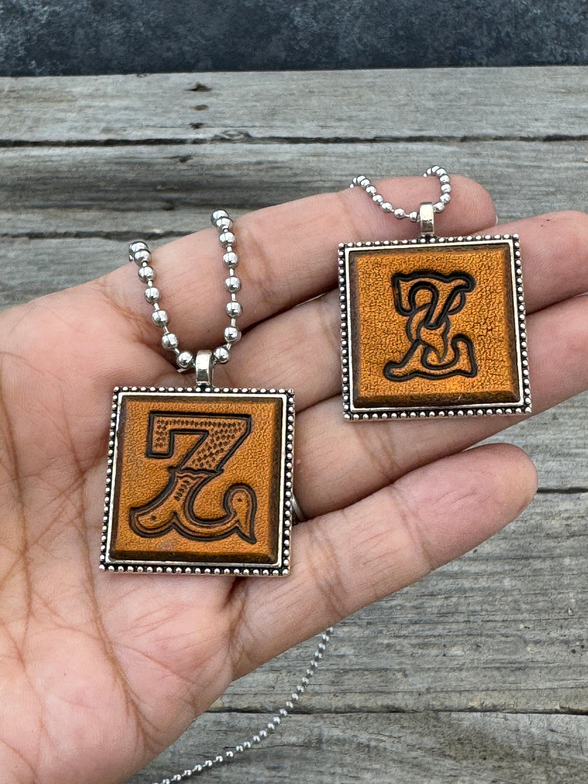 Western Block and Floral Script Letter Z leather necklaces held in hand for size comparison