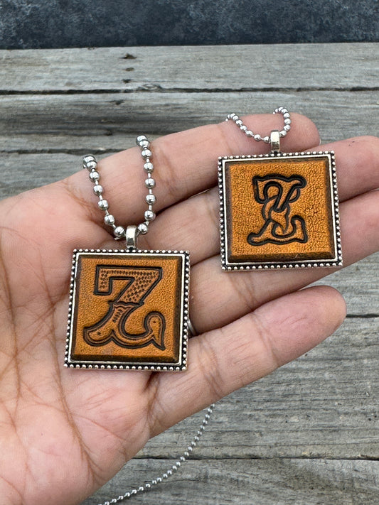 Western Block and Floral Script Letter Z leather necklaces held in hand for size comparison