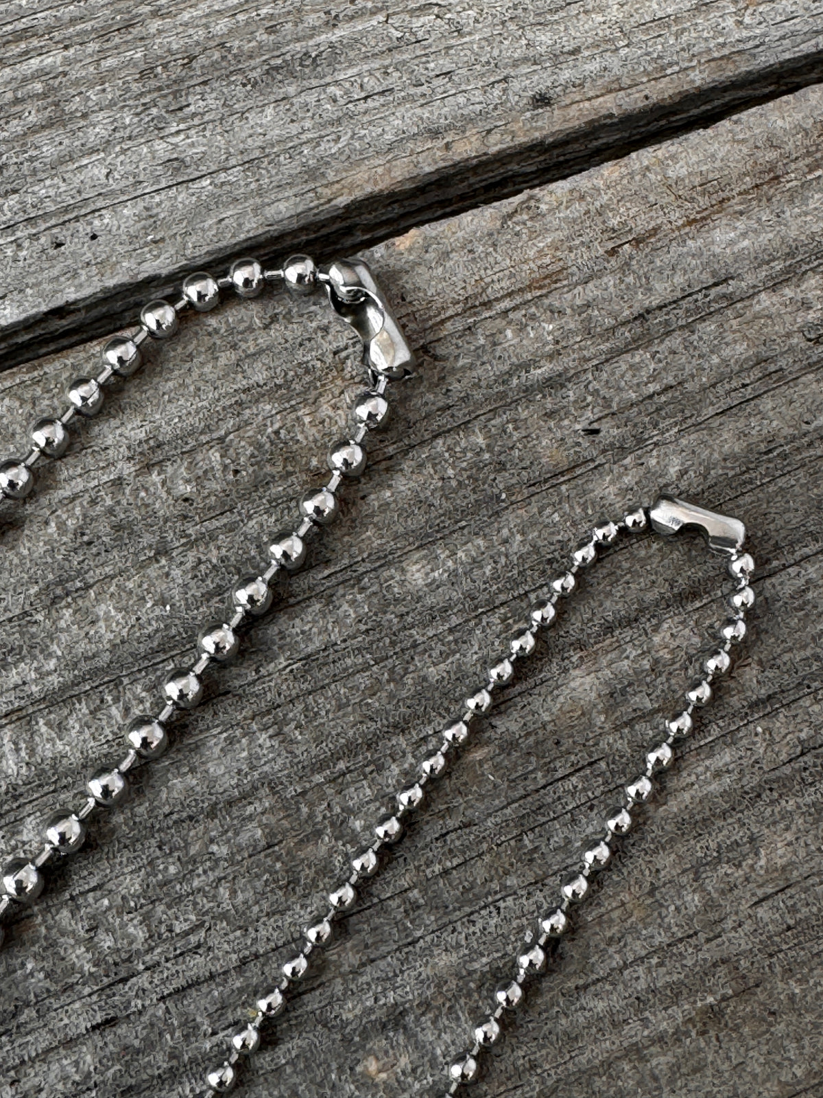 A silver ball chain necklace with a lobster clasp, laid out on a weathered gray wooden surface.