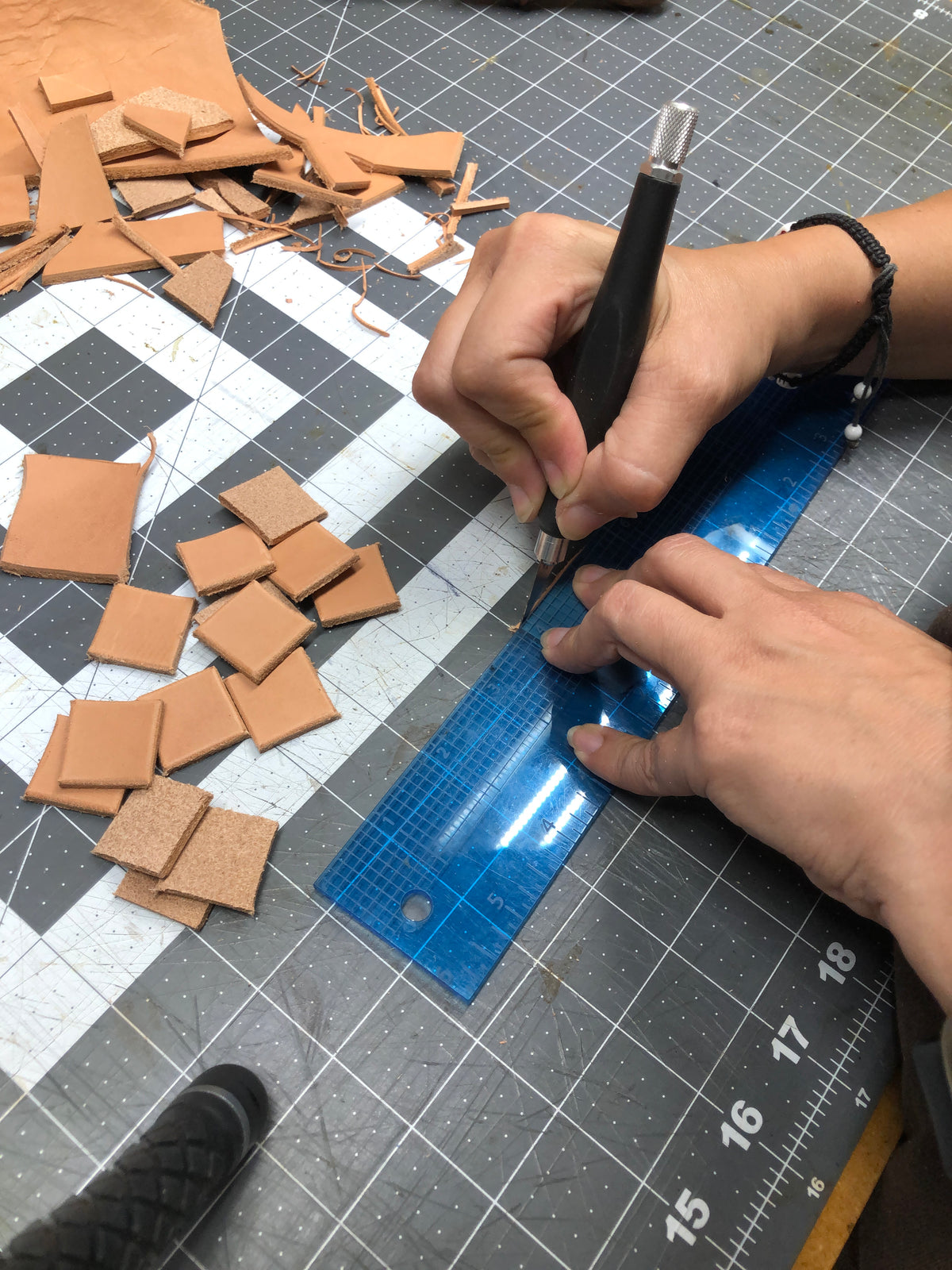 Leather artist hand cutting vegetable-tanned leather pieces for handcrafted initial pendant necklaces