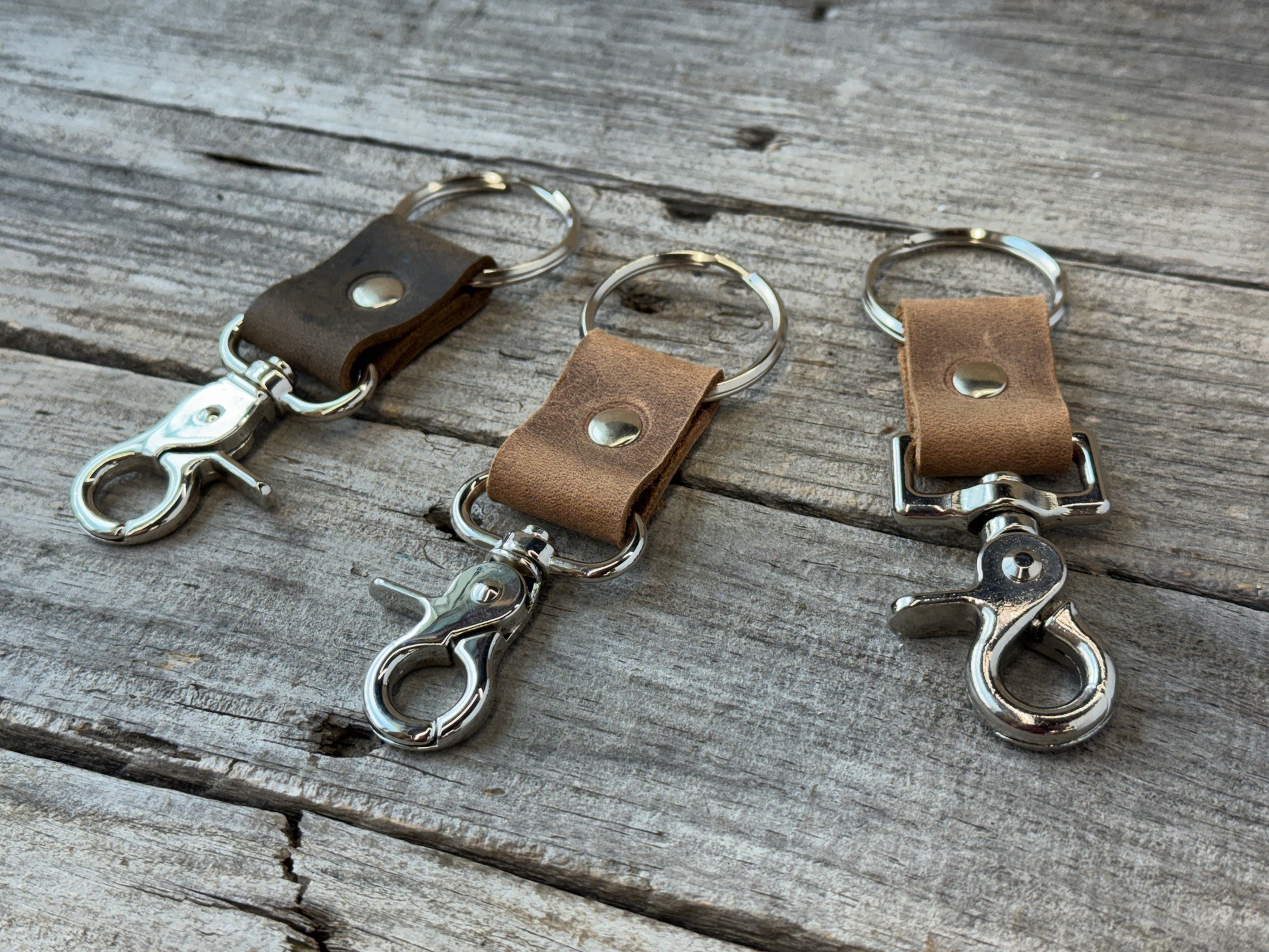 Three leather keychains with metal clasp on a wooden surface