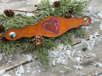 Hand-carved leather cuff bracelet with pink heart and cross design, silver snaps, and pink suede lining, handmade by Cherokee Rose Custom Leather in Texas.