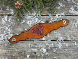 Hand-carved leather cuff bracelet with pink heart and cross design, silver snaps, and pink suede lining, handmade by Cherokee Rose Custom Leather in Texas.