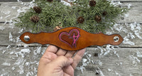 Hand-carved leather cuff bracelet with pink heart and cross design, silver snaps, and pink suede lining, handmade by Cherokee Rose Custom Leather in Texas.