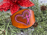 Hand-carved leather cuff bracelet with pink heart and cross design, silver snaps, and pink suede lining, handmade by Cherokee Rose Custom Leather in Texas.