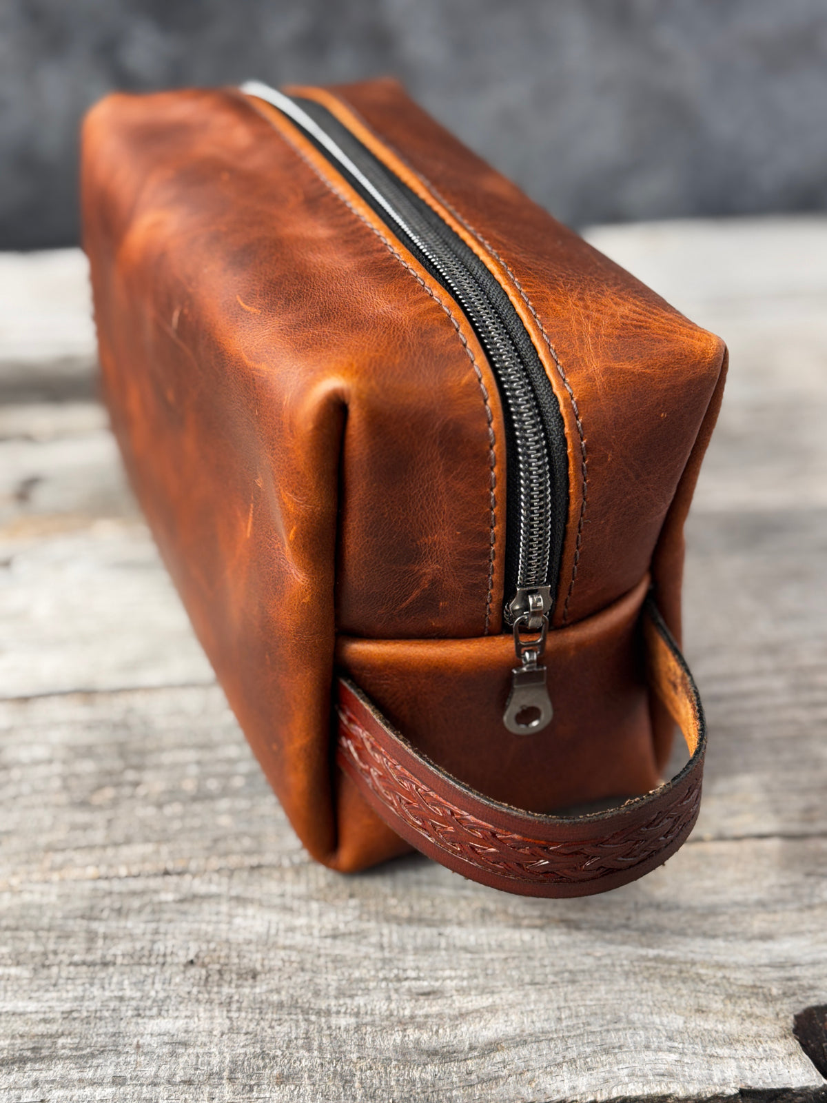 Handmade rustic brown leather Dopp kit standing upright with black zipper and stamped leather handle