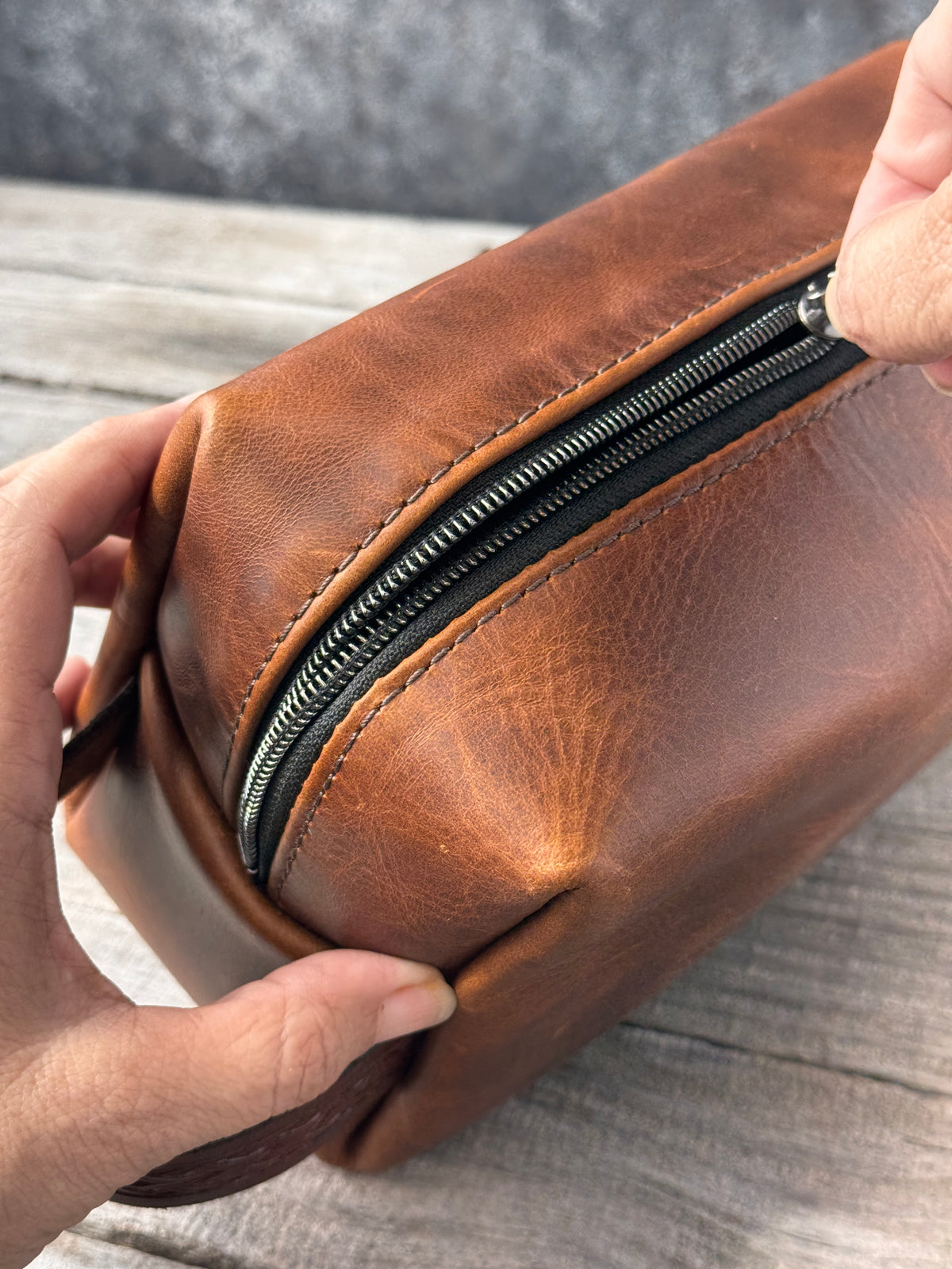 Top angle of brown leather toiletry bag with black zipper and decorative stamped handle