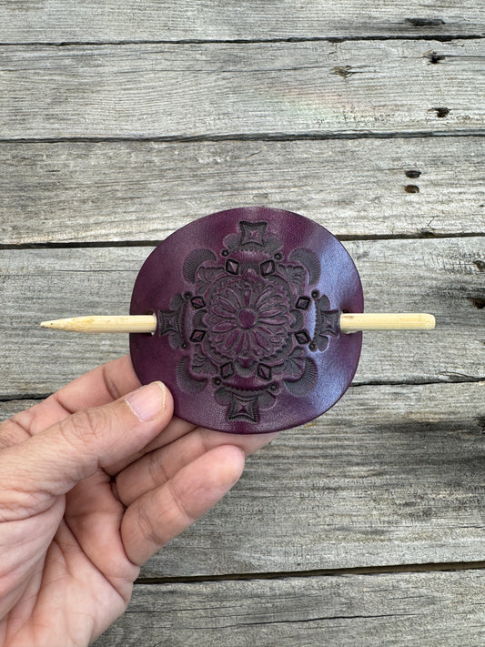 Hand holding a purple decorative object with a wooden stick against a wooden background