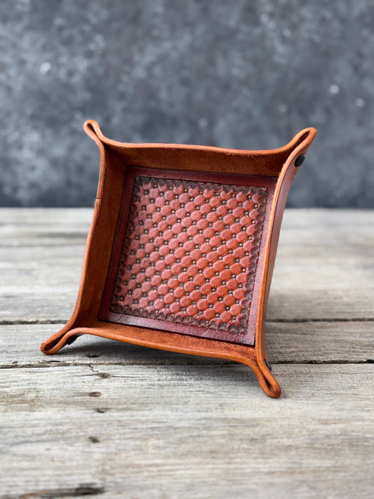Brown leather valet tray with hand stamped quilt pattern on a wooden surface