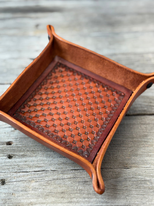 Brown leather valet tray with hand stamped quilt pattern on a wooden background