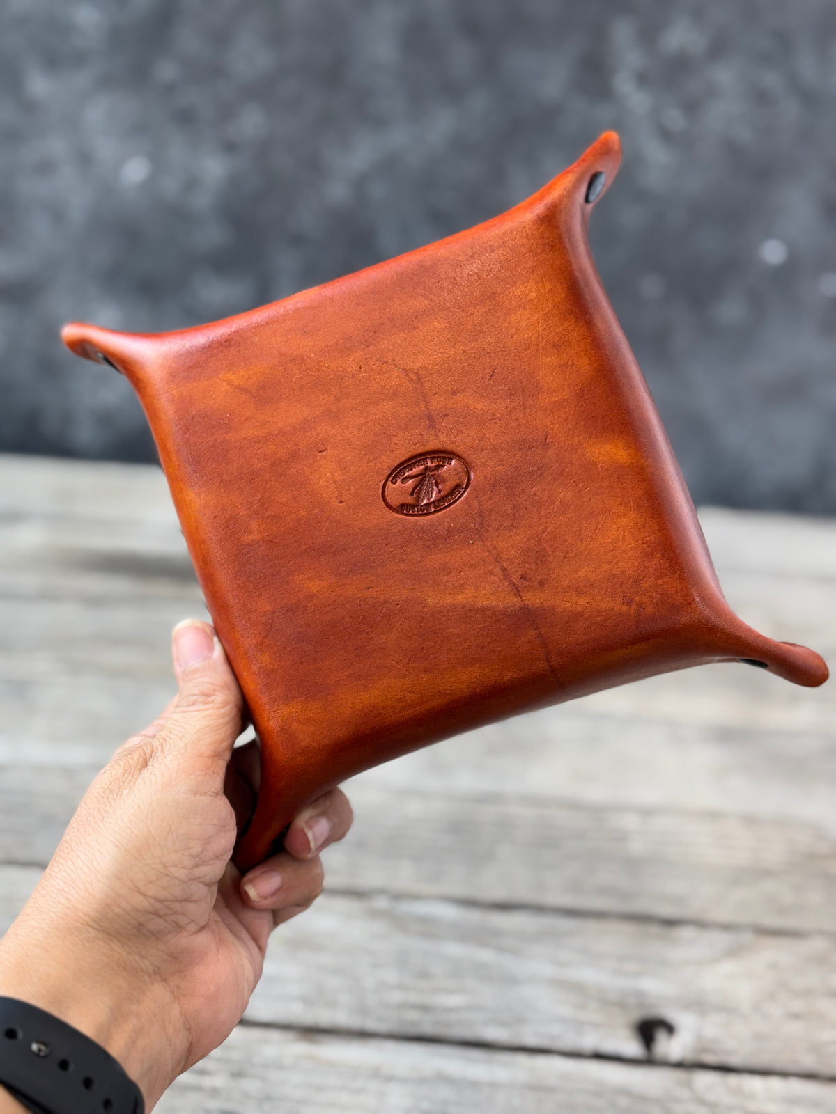 Brown leather valet tray held by a hand on a wooden surface with a blurred background