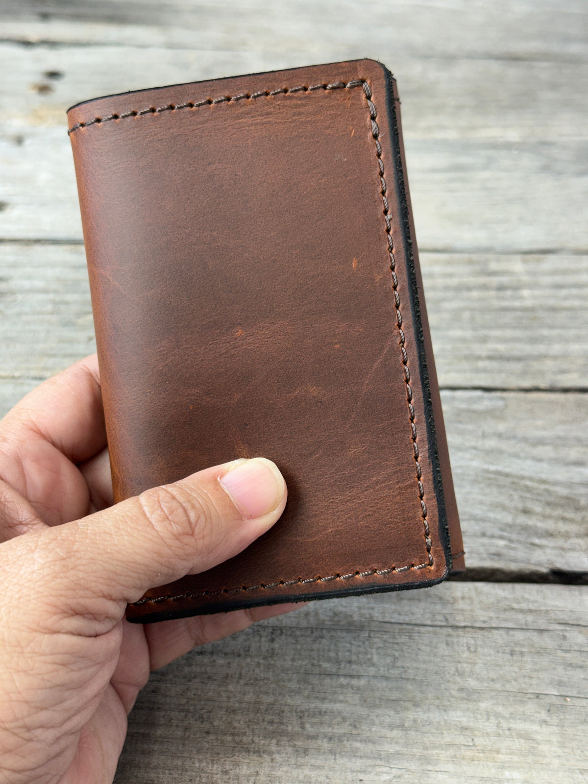 Rustic brown oil tanned leather trifold wallet held in hand