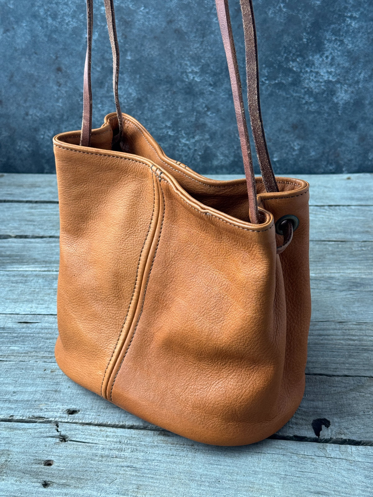 Handmade saddle tan leather bucket bag angled view with stitched seams and shoulder straps
