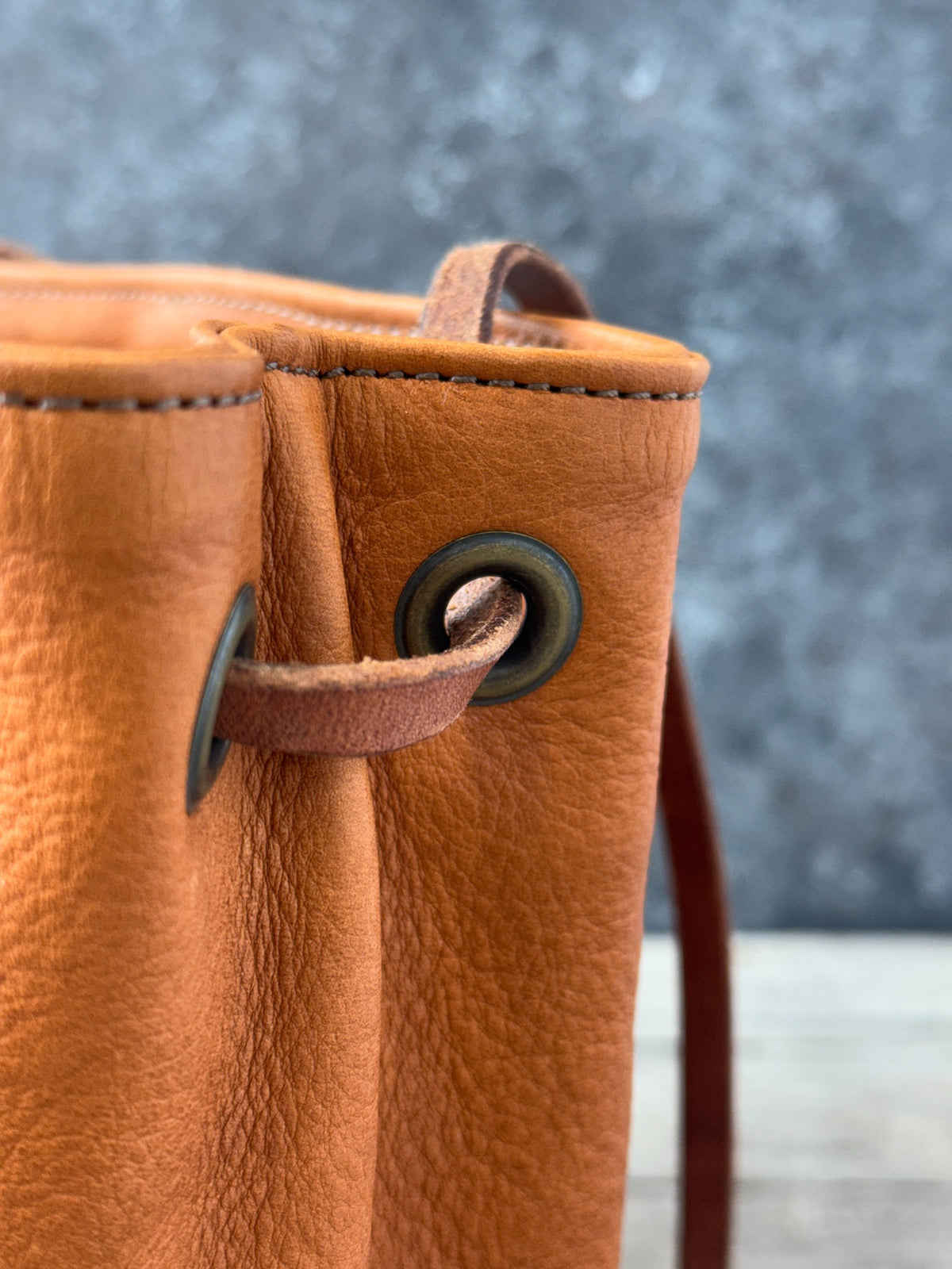 Leather bucket bag close-up of brass-tone grommets and shoulder strap attachment
