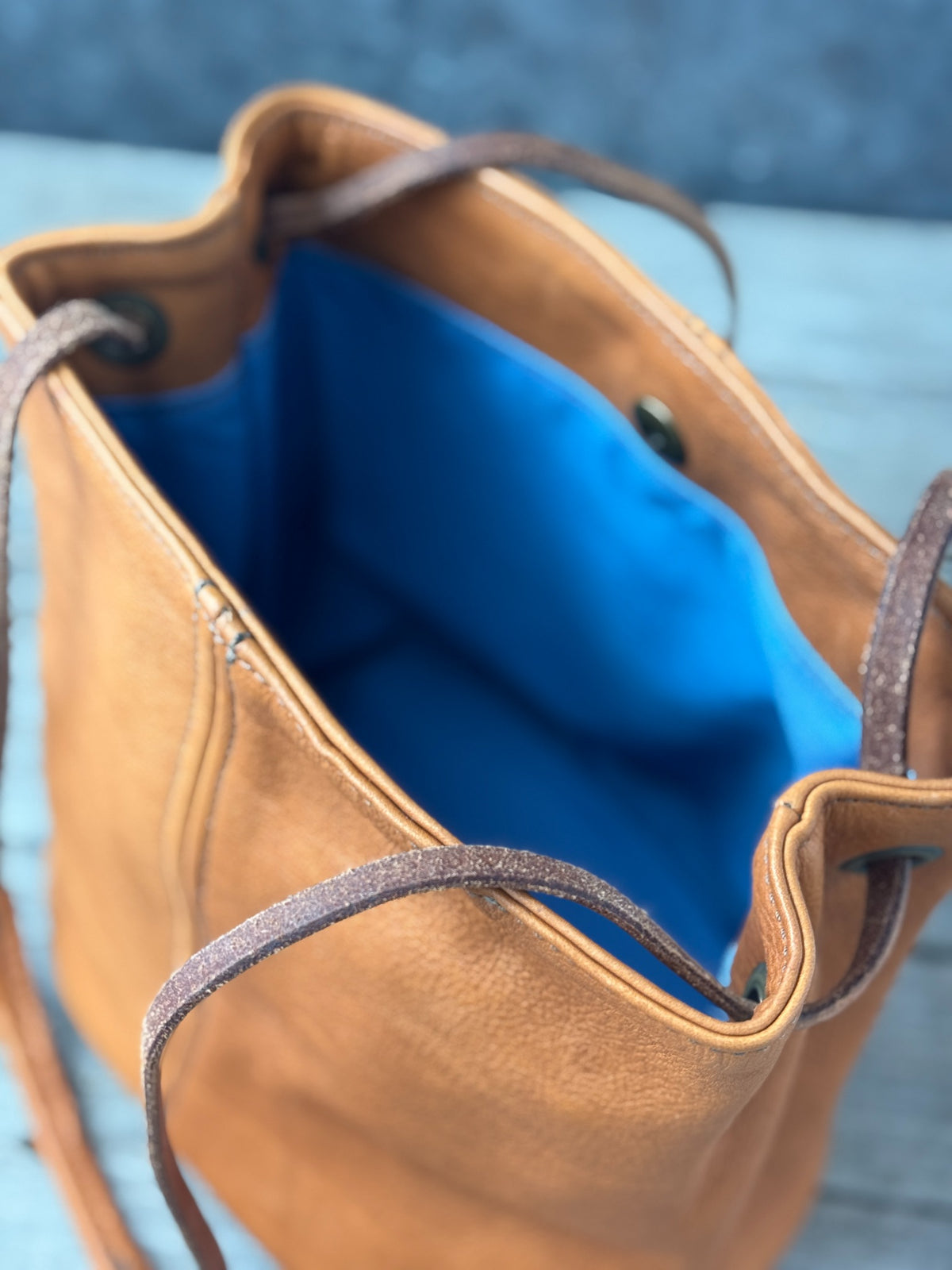 Open saddle tan leather bucket bag with vibrant blue canvas lining