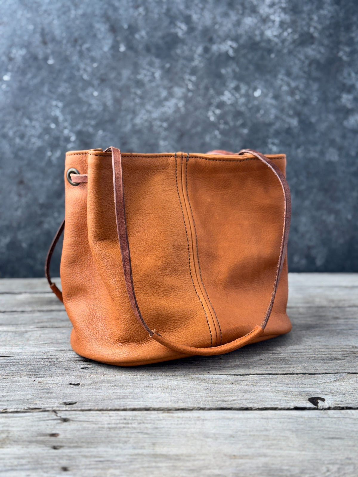 Handmade saddle tan leather bucket bag showing stitched shoulder strap