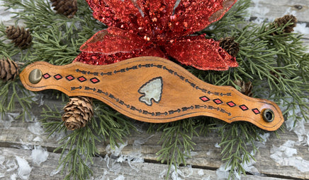 Hand-tooled leather cuff bracelet with arrowhead centerpiece, red diamond accents, and antique brass snaps, handmade by Cherokee Rose Custom Leather in Texas.