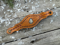 Hand-tooled leather cuff bracelet with arrowhead centerpiece, red diamond accents, and antique brass snaps, handmade by Cherokee Rose Custom Leather in Texas.