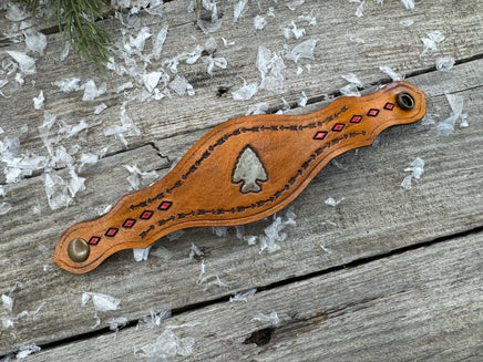 Hand-tooled leather cuff bracelet with arrowhead centerpiece, red diamond accents, and antique brass snaps, handmade by Cherokee Rose Custom Leather in Texas.