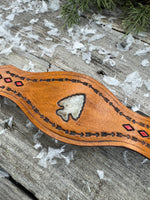 Hand-tooled leather cuff bracelet with arrowhead centerpiece, red diamond accents, and antique brass snaps, handmade by Cherokee Rose Custom Leather in Texas.