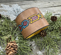 Wide hand-carved leather cuff bracelet with turquoise arrow and yellow tribal design, antique copper snaps, and yellow suede lining, handmade by Cherokee Rose Custom Leather.
