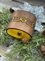 Wide hand-carved leather cuff bracelet with turquoise arrow and yellow tribal design, antique copper snaps, and yellow suede lining, handmade by Cherokee Rose Custom Leather.