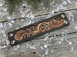 Wide hand-carved leather cuff bracelet with turquoise accents, feather details, and silver snaps, handmade by Cherokee Rose Custom Leather in East Texas.