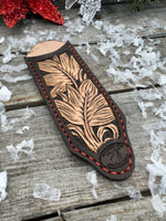 Hand tooled leather cast iron skillet handle cover in chocolate brown with carved leaf design and red stitching, handmade by Cherokee Rose Custom Leather in East Texas.