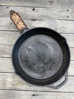Hand tooled leather cast iron skillet handle cover in chocolate brown with carved leaf design and red stitching, handmade by Cherokee Rose Custom Leather in East Texas.