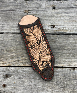 Decorative leather knife sheath with feather design on a wooden surface