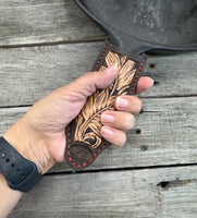 Hand tooled leather cast iron skillet handle cover in chocolate brown with carved leaf design and red stitching, handmade by Cherokee Rose Custom Leather in East Texas.