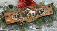 Wide hand-painted leather cuff bracelet with wild paint pony, sunflowers, and antique brass snaps, handmade by Cherokee Rose Custom Leather in East Texas.