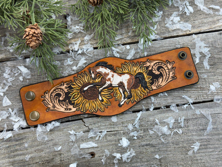 Wide hand-painted leather cuff bracelet with wild paint pony, sunflowers, and antique brass snaps, handmade by Cherokee Rose Custom Leather in East Texas.